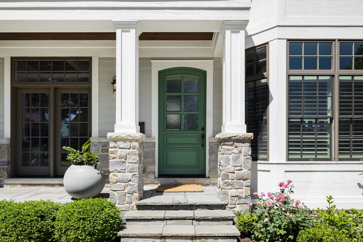 Front porch of a modern farmhouse with a green front door and stone pillars